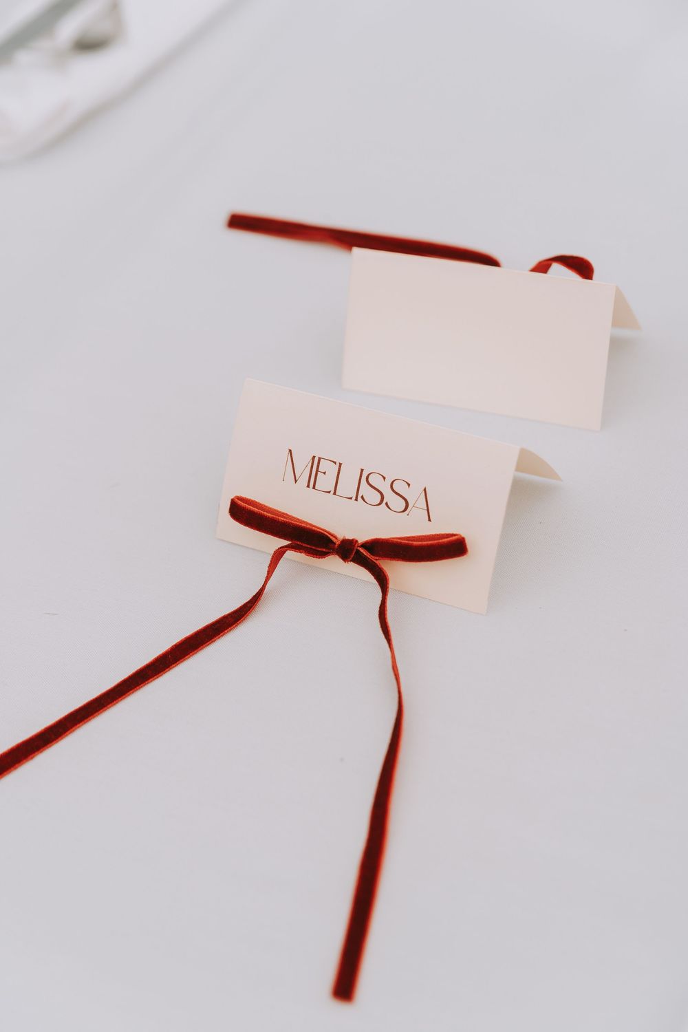 Elegant wedding place card for Melissa with red velvet ribbon bow on white background.