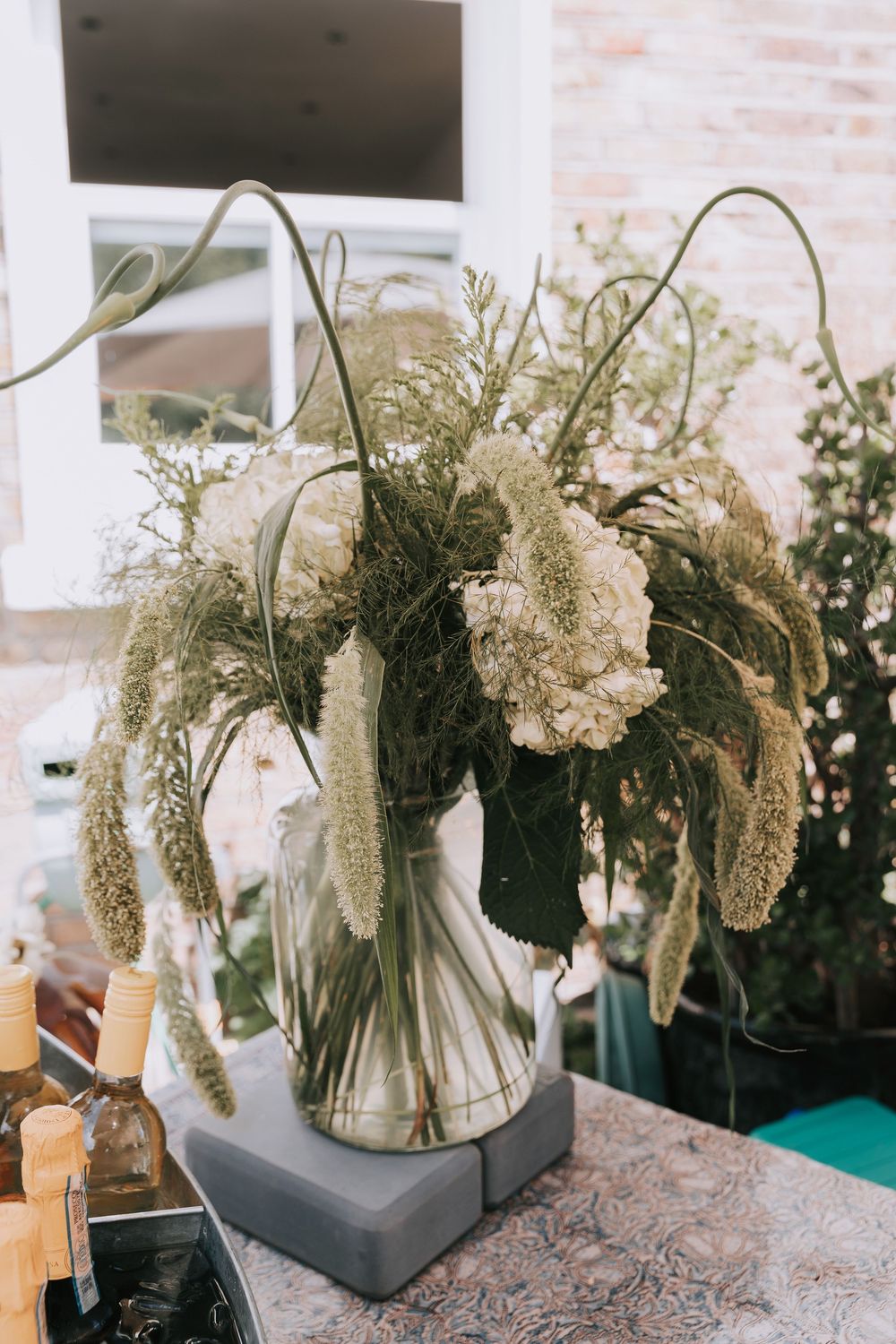 Elegant floral arrangement with white hydrangeas, pampas grass, and greenery in a glass vase on a marble stand.