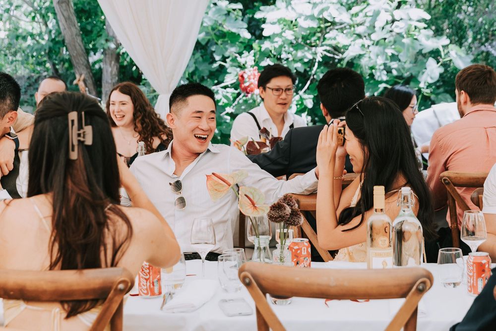 Smiling wedding guests toasting and celebrating at an elegant outdoor garden reception dinner table.