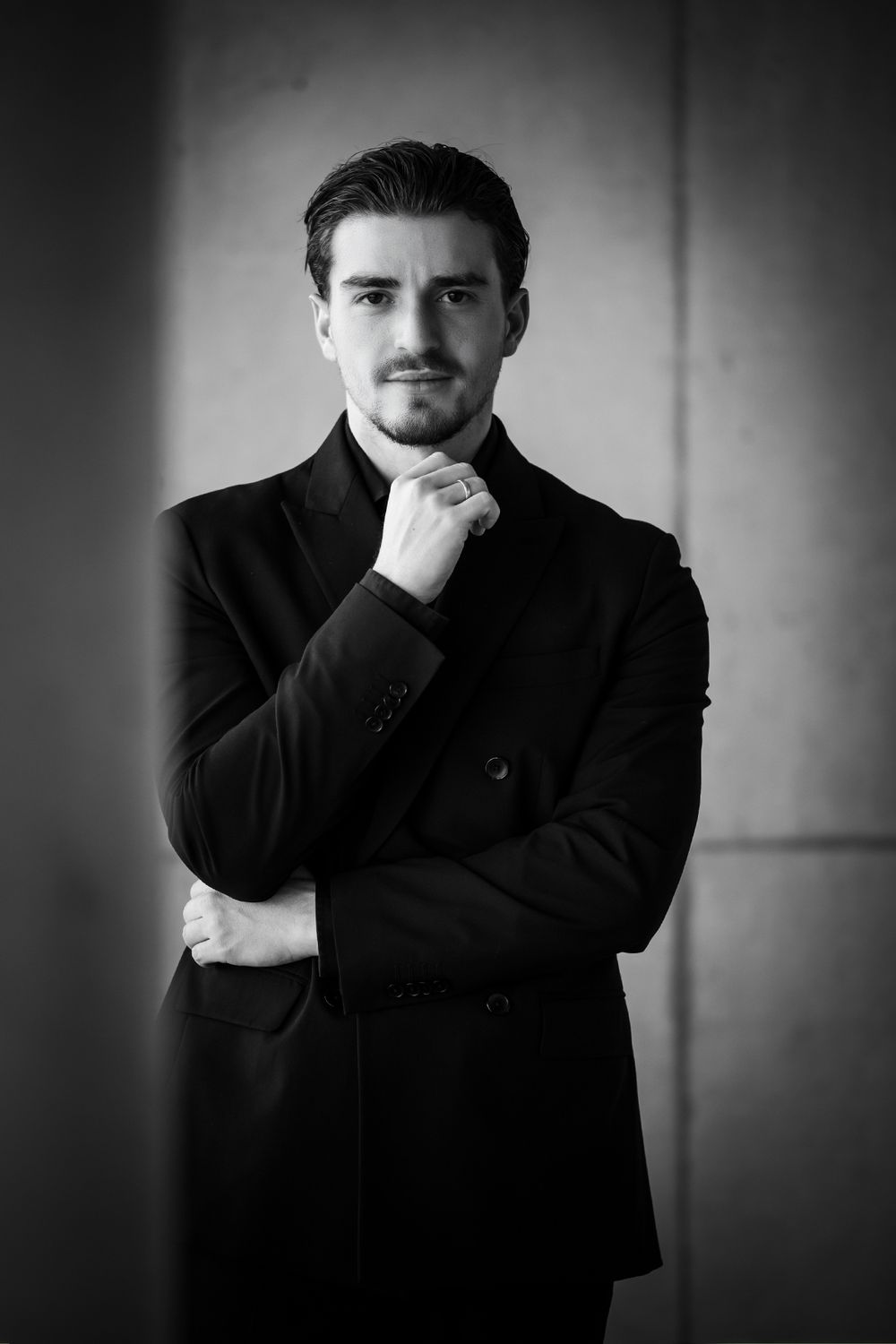 Schwarz-weißes Businessporträt eines Mannes mit verschränkten Armen, Hand am Kinn und ernstem Blick in die Kamera.