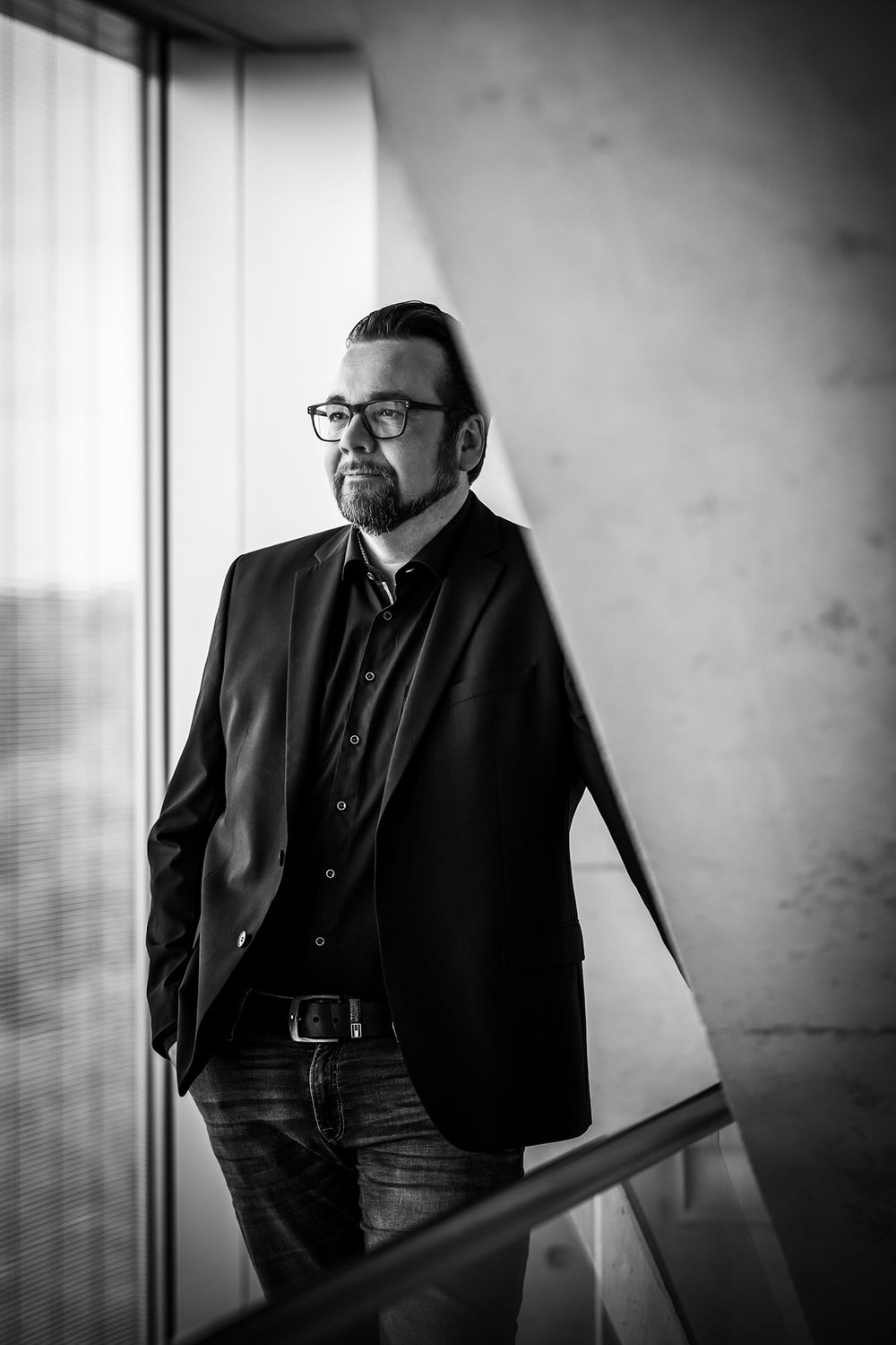 Schwarz-weißes Businessporträt eines Mannes mit lässiger Haltung, einer Hand in der Hosentasche und Blick zur Seite.
