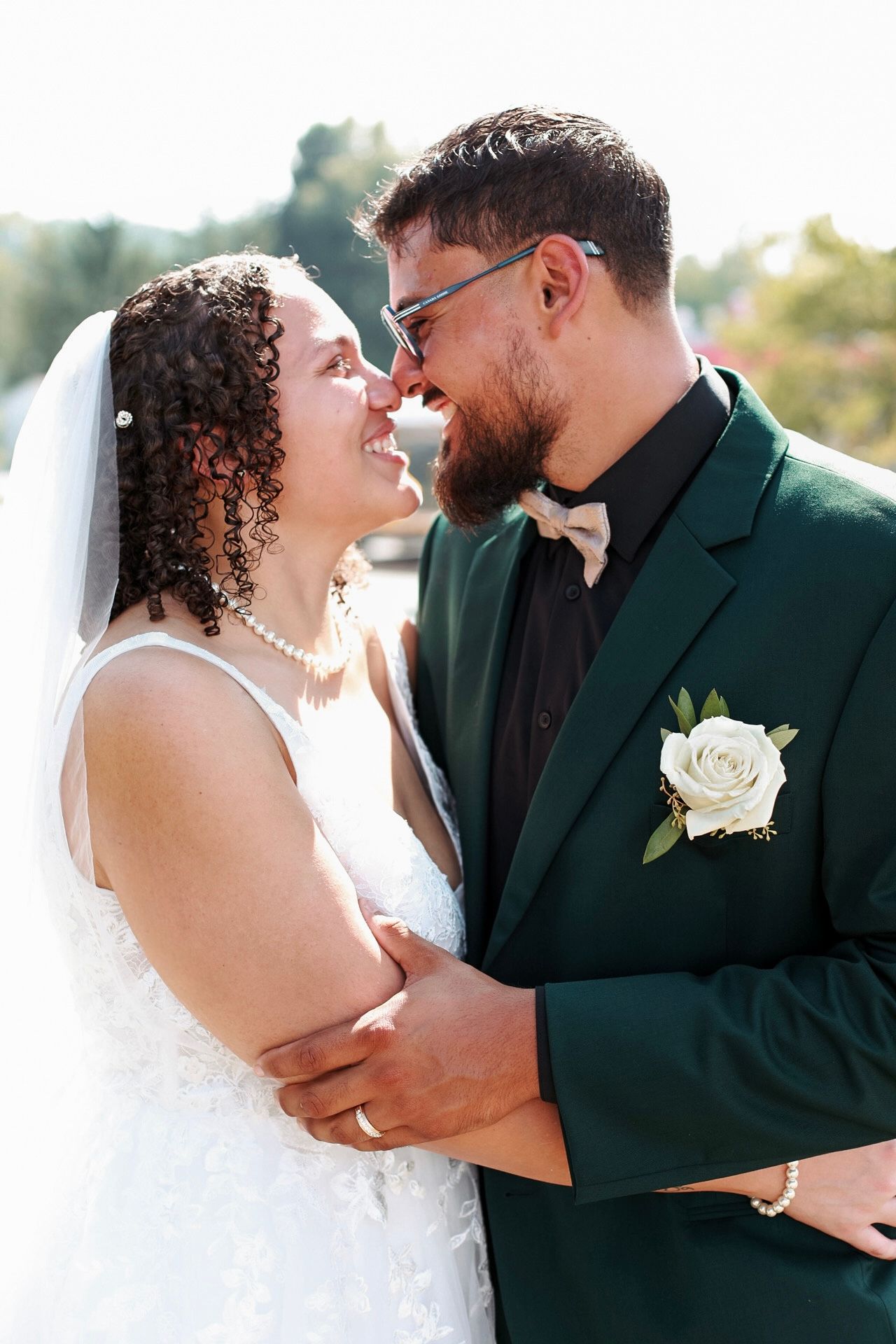 A joyful bride and groom share a romantic moment, nearly kissing, as she wears a white gown and he a green suit.