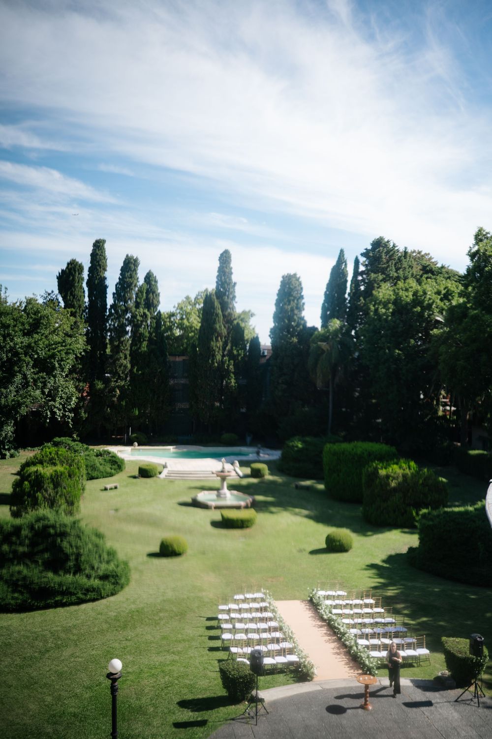 Elegant outdoor wedding ceremony setup with white chairs in lush garden.