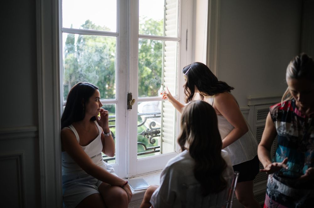 Bridesmaids gathering by French windows during wedding morning preparations.