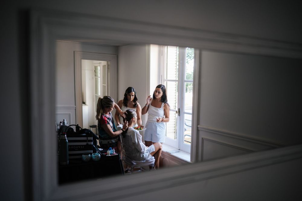 Mirror reflection of bridesmaids getting hair and makeup done before a wedding.