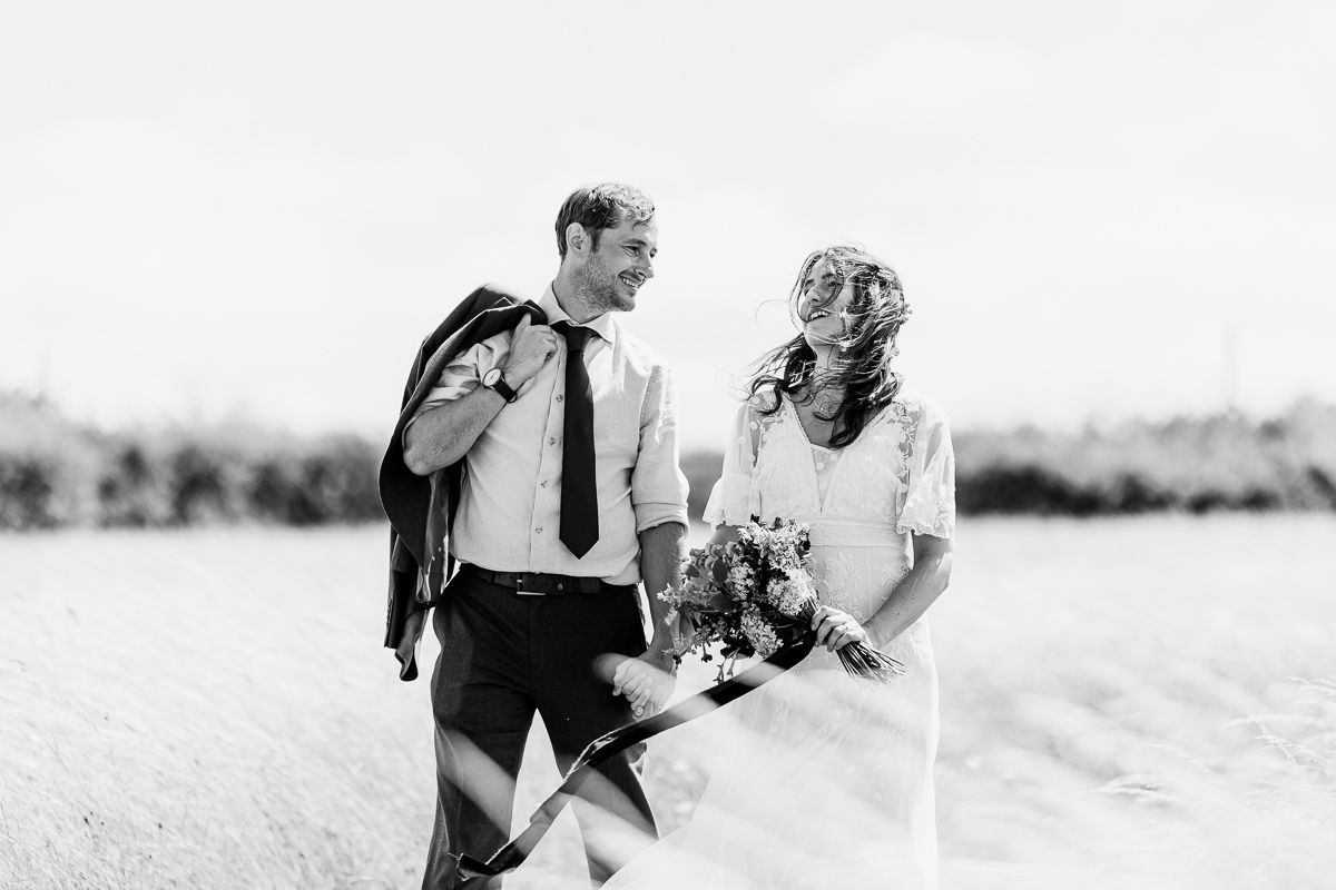 Black and white photo of a bride and groom laughing together in an open field, bride holding a bouquet.