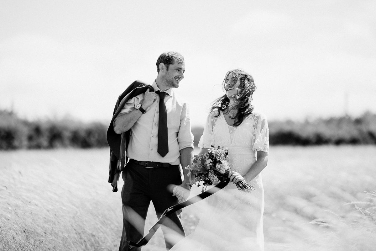 Black and white photo of a bride and groom smiling at each other in a field, bride holding a bouquet.