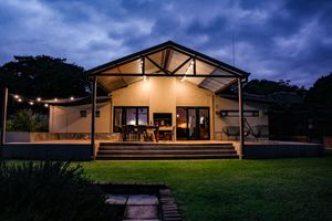 Cozy Unique Stay illuminated with string lights at dusk, featuring a covered patio and lush green lawn.