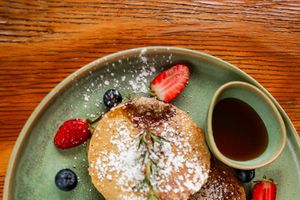 Fluffy pancakes topped with powdered sugar, fresh strawberries, blueberries, and served with maple syrup in a Unique Stay's Bistro.