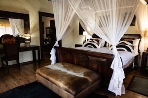Luxury safari bedroom with canopy bed, white drapes, hardwood floors, and cowhide ottoman in elegant lodge suite.