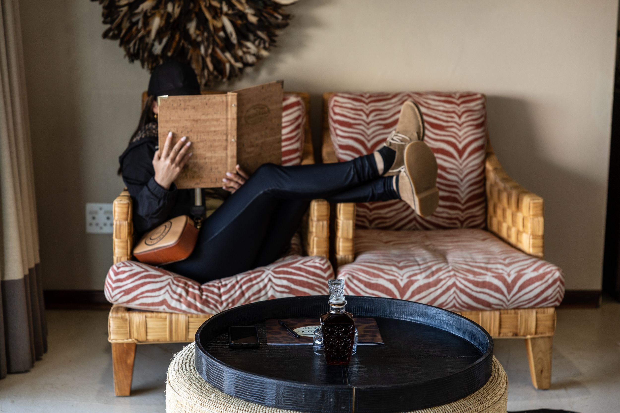 Person relaxing on a zebra-print sofa reading a book, with feet up, relaxing in a Luxury Safari Lodge suite.