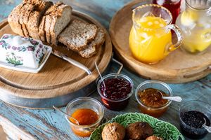 Rustic breakfast spread with home made bread, assorted jams, butter, and orange juice on a wooden tray.