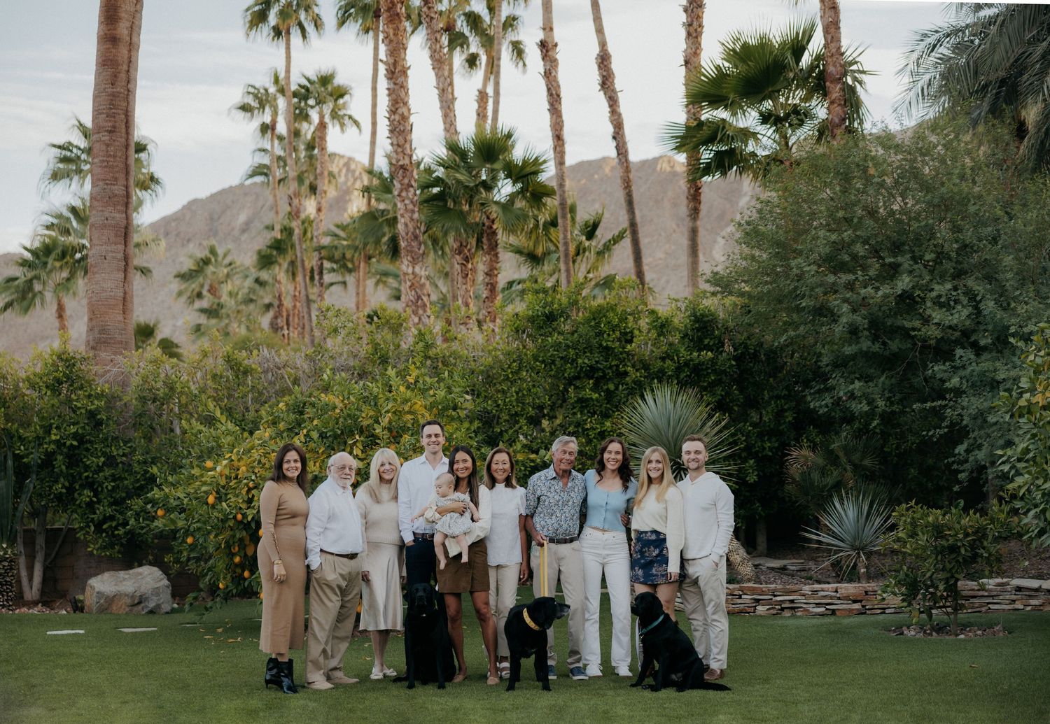Family group photo on green lawn with palm trees and mountains in background on sunny day.