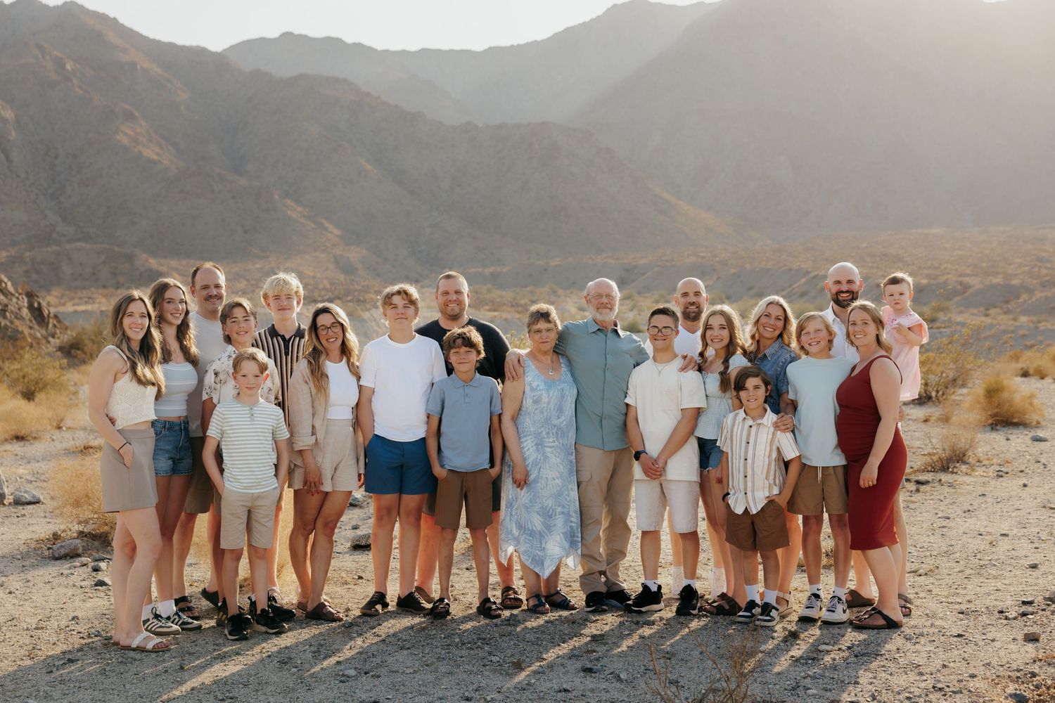 Large family group portrait outdoors with mountain backdrop in desert landscape during golden hour.
