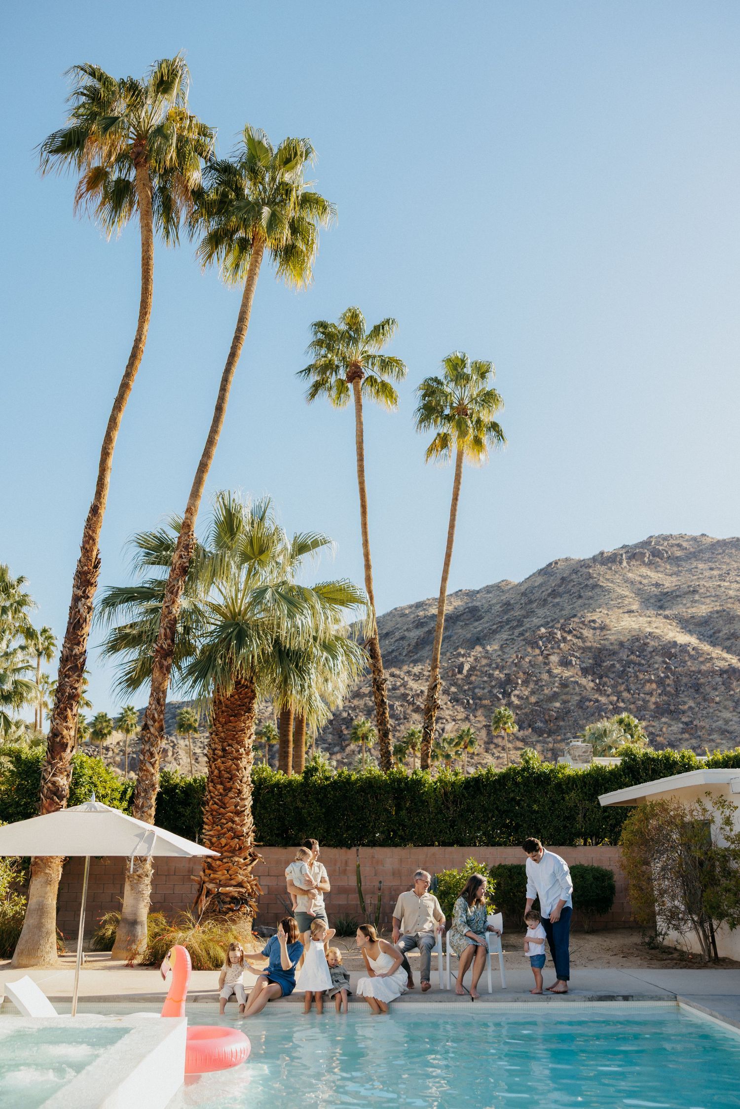 Family gathering poolside with tall palm trees and mountain backdrop on a sunny day in Palm Springs.