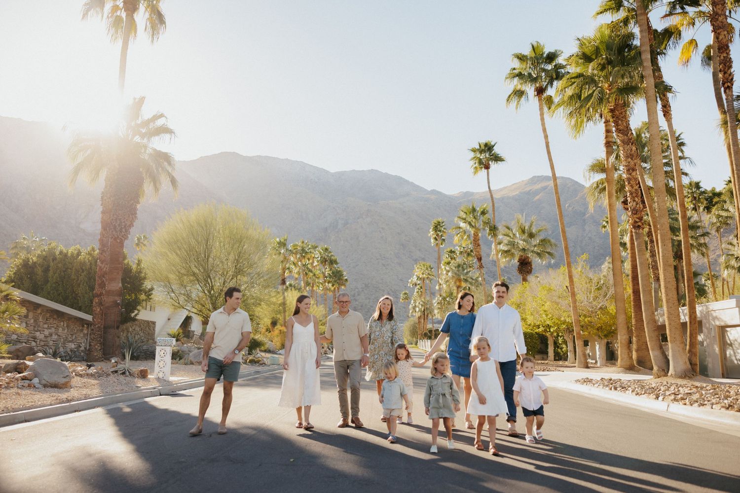 Large family walking together on a sunny Palm Springs street surrounded by tall palm trees and mountain backdrop.