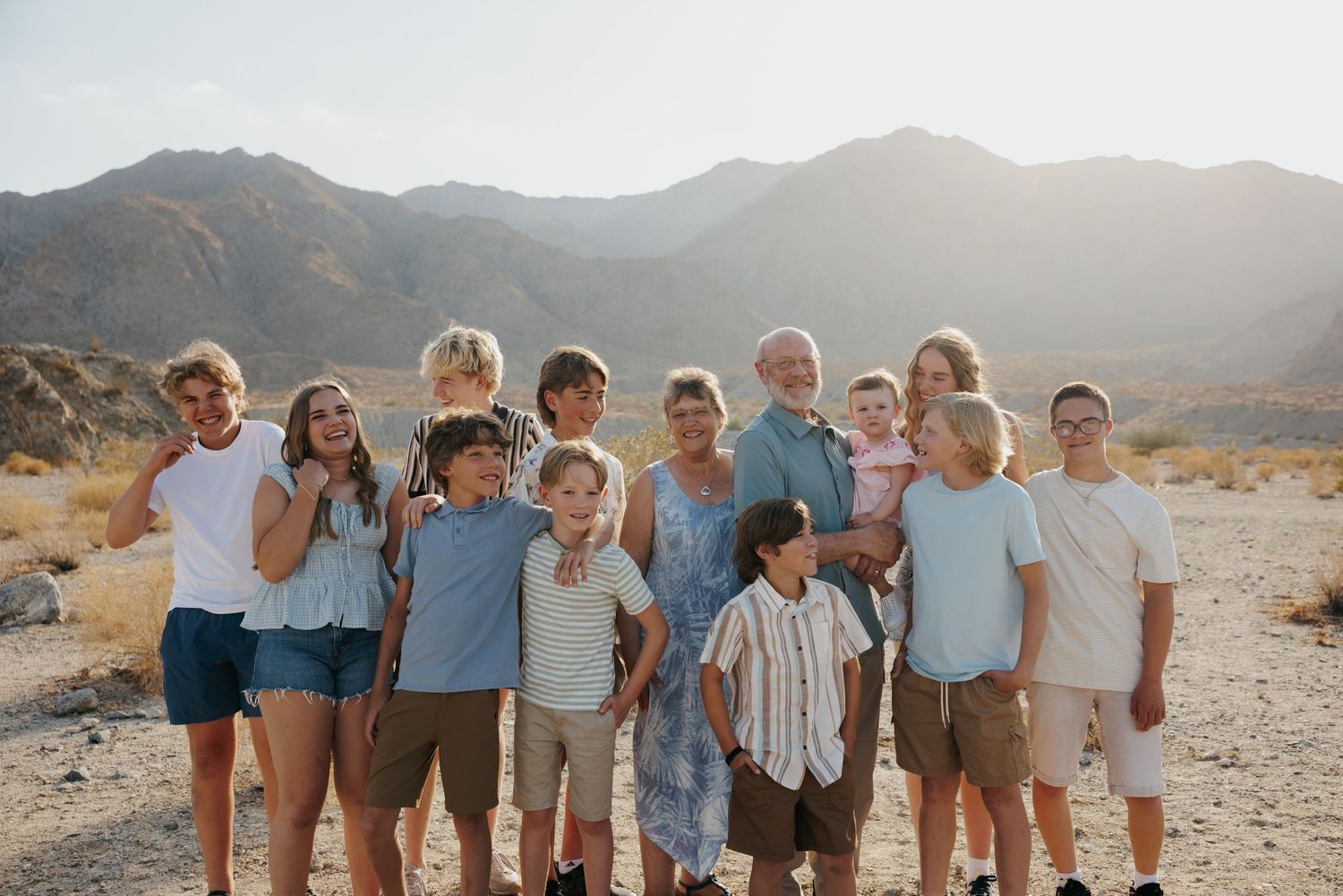 Large family group smiling together in a sunny desert landscape with mountains in the background.