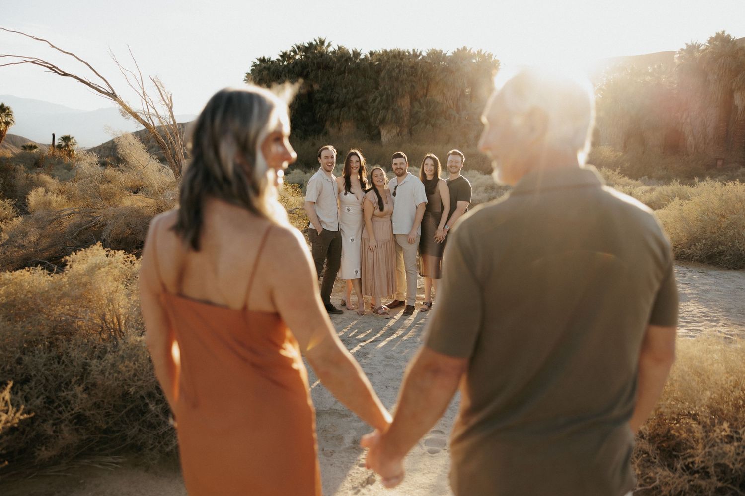 Couple holding hands walking toward a group of friends in a desert landscape at golden hour sunset.