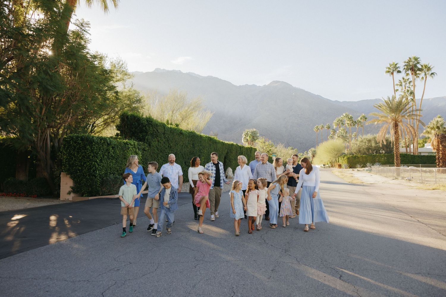 Large family group walking together on a sunny street with lush greenery and mountain backdrop in Palm Springs.