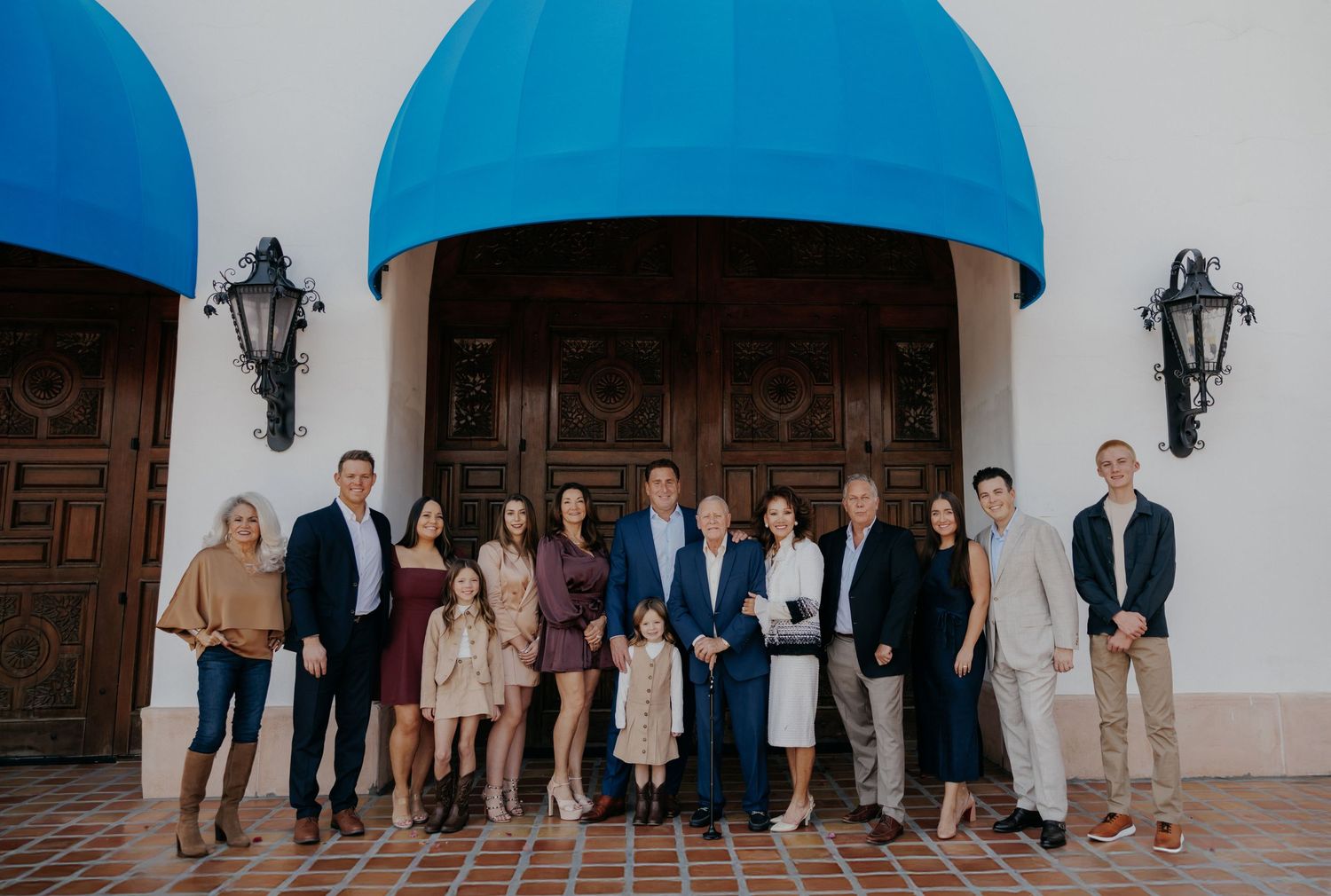 Large family group portrait posed under blue awning outside elegant building with wooden doors.