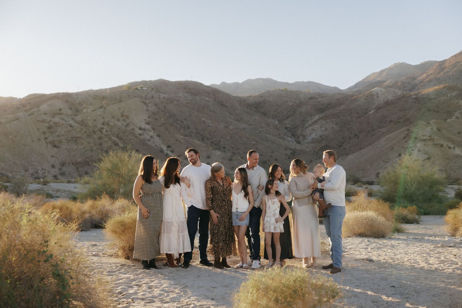 Large family group photo in desert landscape with mountains at golden hour, wearing neutral tones.
