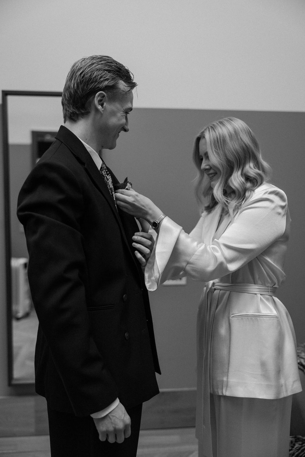 Black and white photo of a bride adjusting the groom's tie before their wedding ceremony.