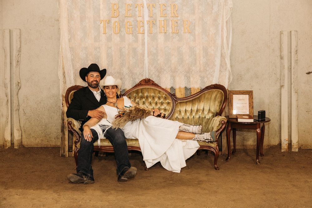 Newlywed couple relaxing on vintage gold sofa in rustic barn wedding venue with Better Together backdrop.