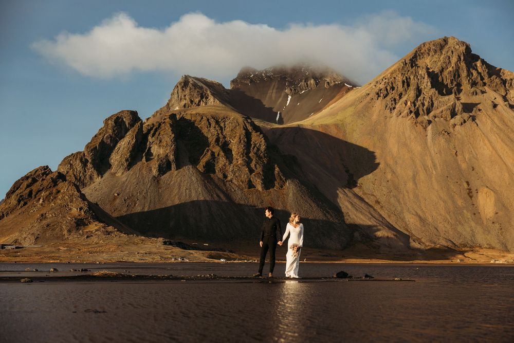 Couple in wedding attire holds hands before dramatic Vestrahorn mountain landscape in Iceland.