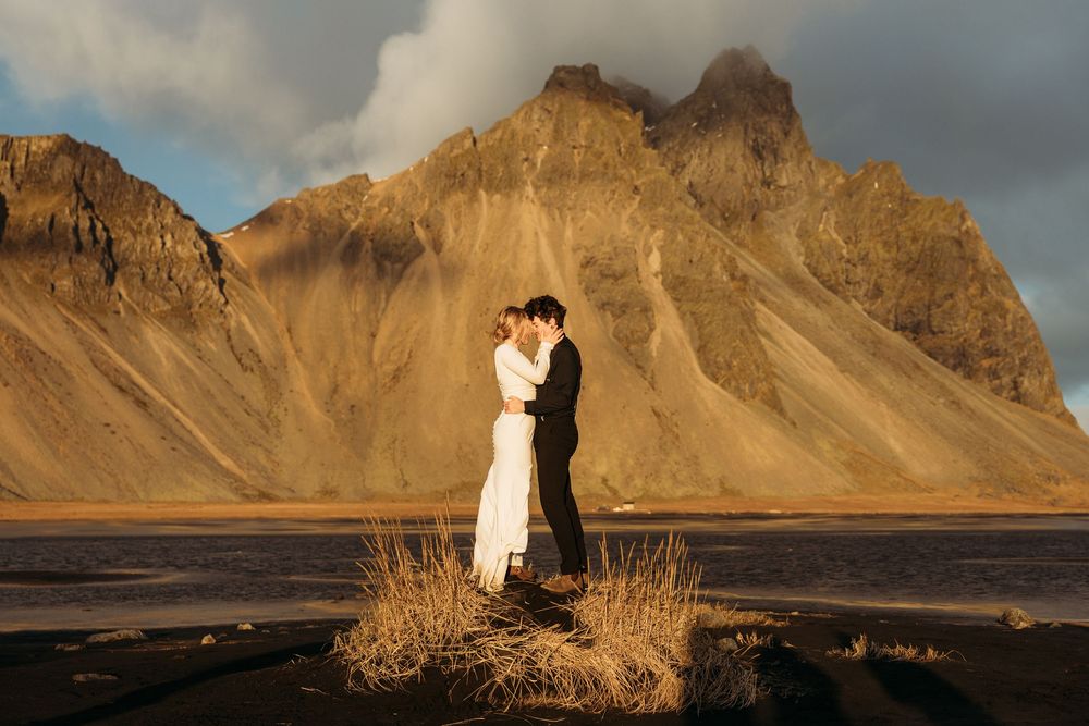 Couple embracing at golden hour with dramatic Vestrahorn mountain backdrop in Iceland during elopement wedding.