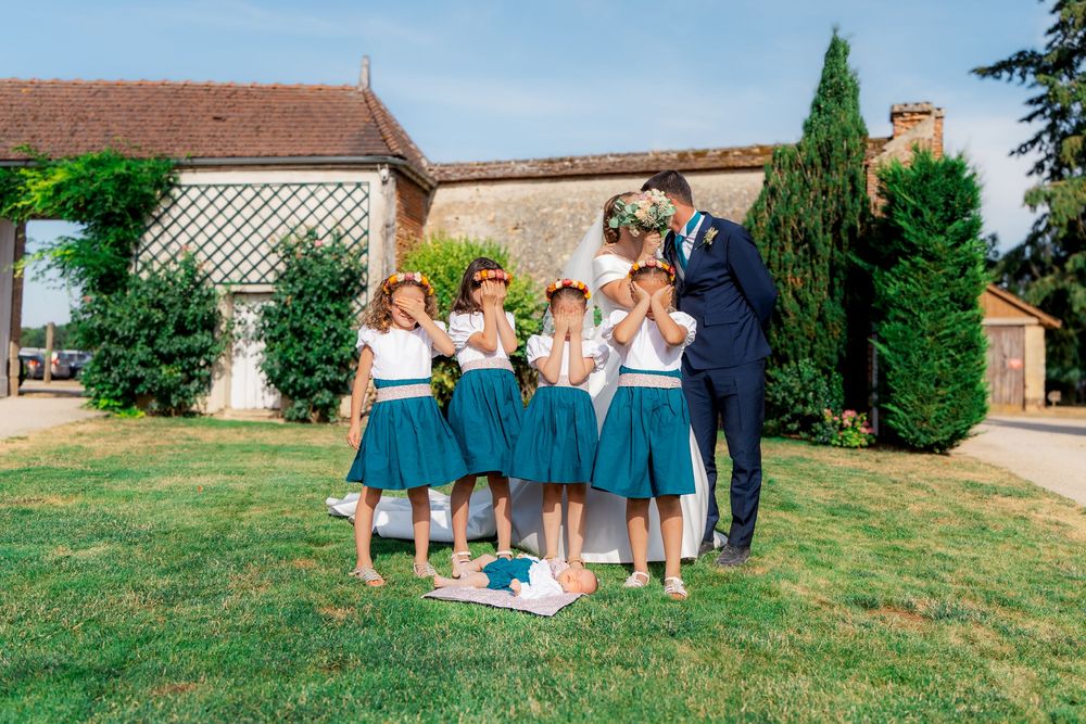 Groom in navy suit with flower girls in teal dresses celebrating outdoors at a French countryside wedding venue.