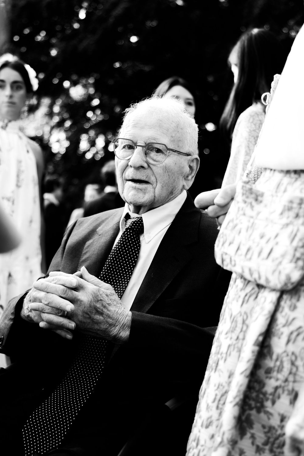 Elderly man in suit and tie with glasses, smiling at outdoor event in black and white photo.