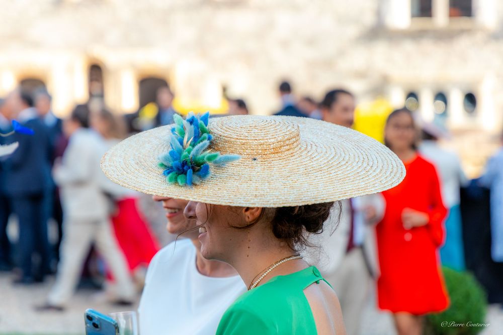 Woman wearing a wide-brim straw hat with blue floral accent at an outdoor social gathering.