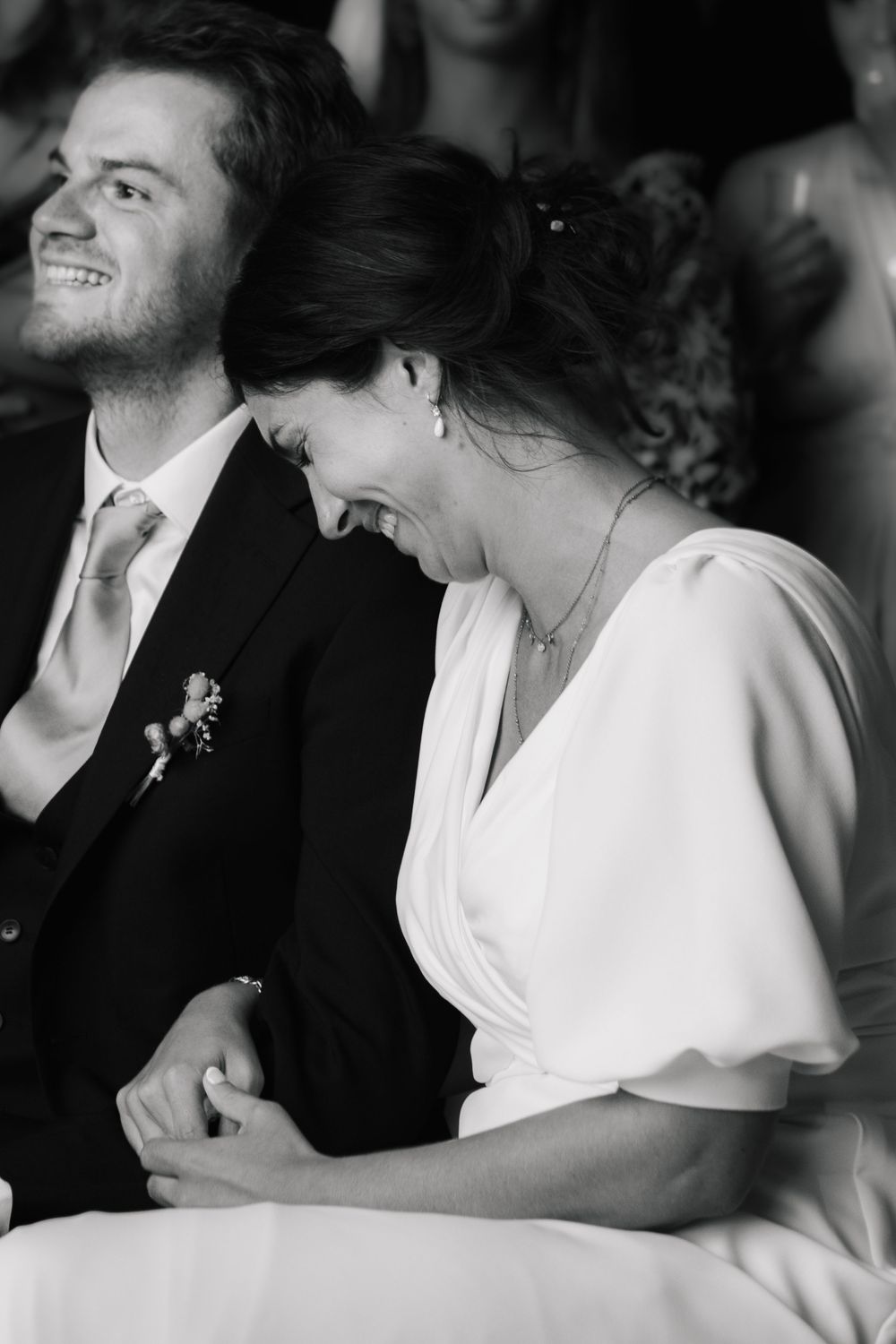 Black and white photo of a laughing bride and groom holding hands during their wedding ceremony.