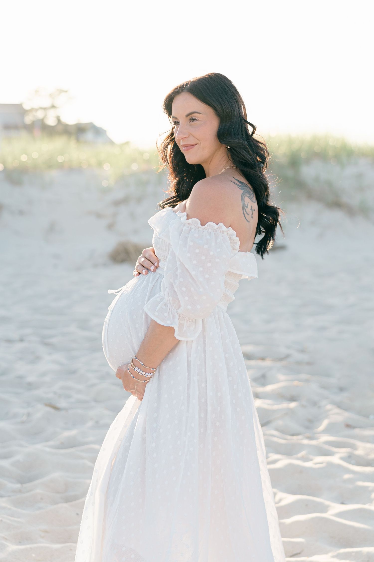 Pregnant woman in a flowy white dress at golden hour for a Manasquan beach maternity session.