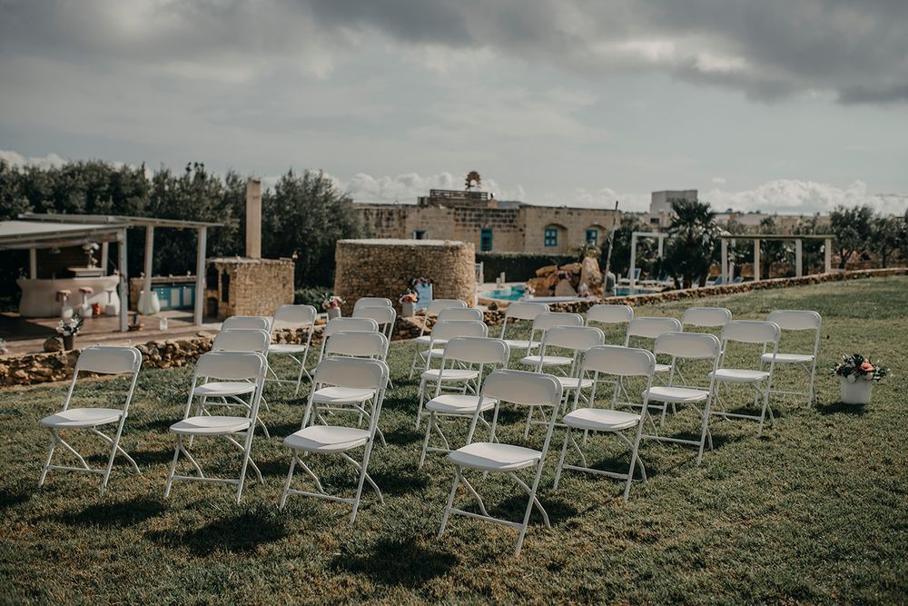 White folding chairs arranged in rows on green grass for an outdoor wedding ceremony at a rustic stone venue.
