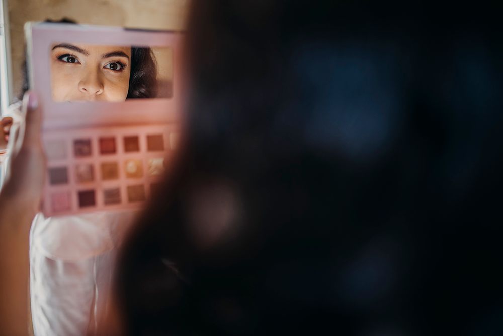 Woman holding a makeup eyeshadow palette reflecting her face in a mirror during a beauty session.
