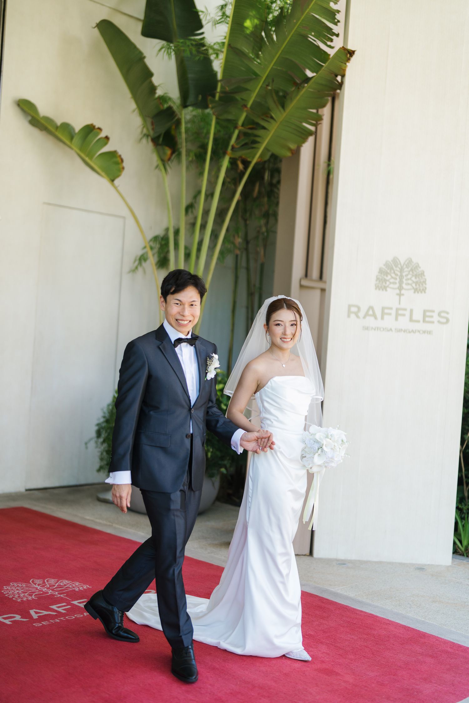 Bride and groom embracing by reflective pool before elegant building with arched windows and terracotta roof.