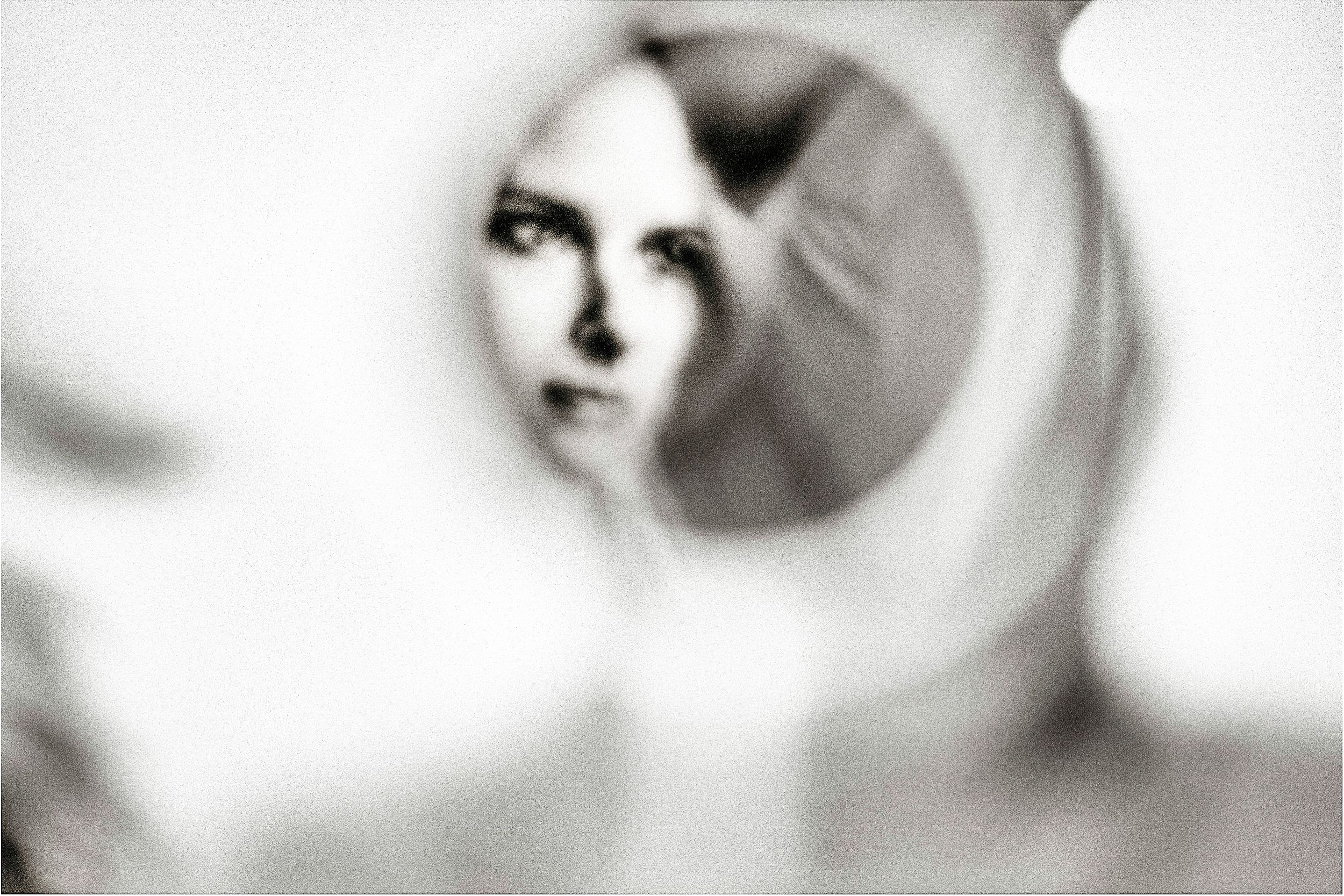 Black and white photo of a woman's face reflected in a small round mirror, artistic blurred bokeh effect.