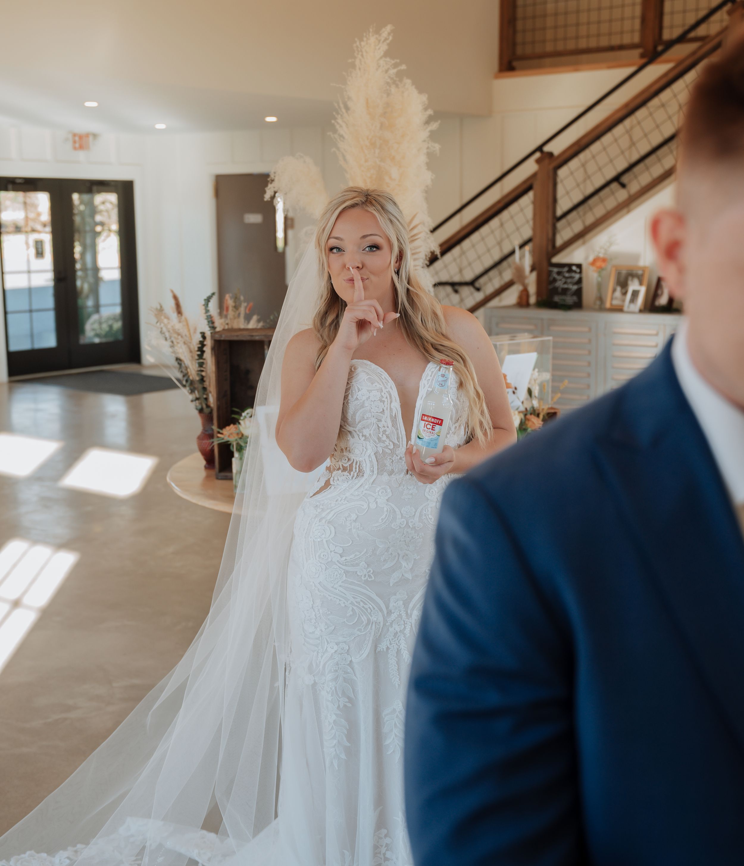 Bride playfully gestures shh while sneaking up on groom during a fun first look wedding moment.