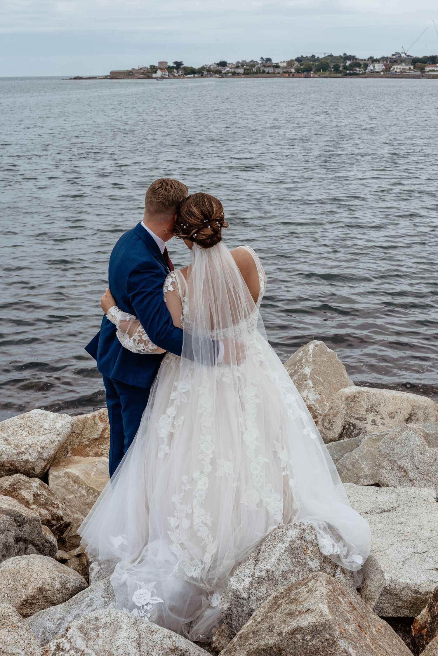 A couple shares an intimate moment on coastal rocks overlooking the ocean.