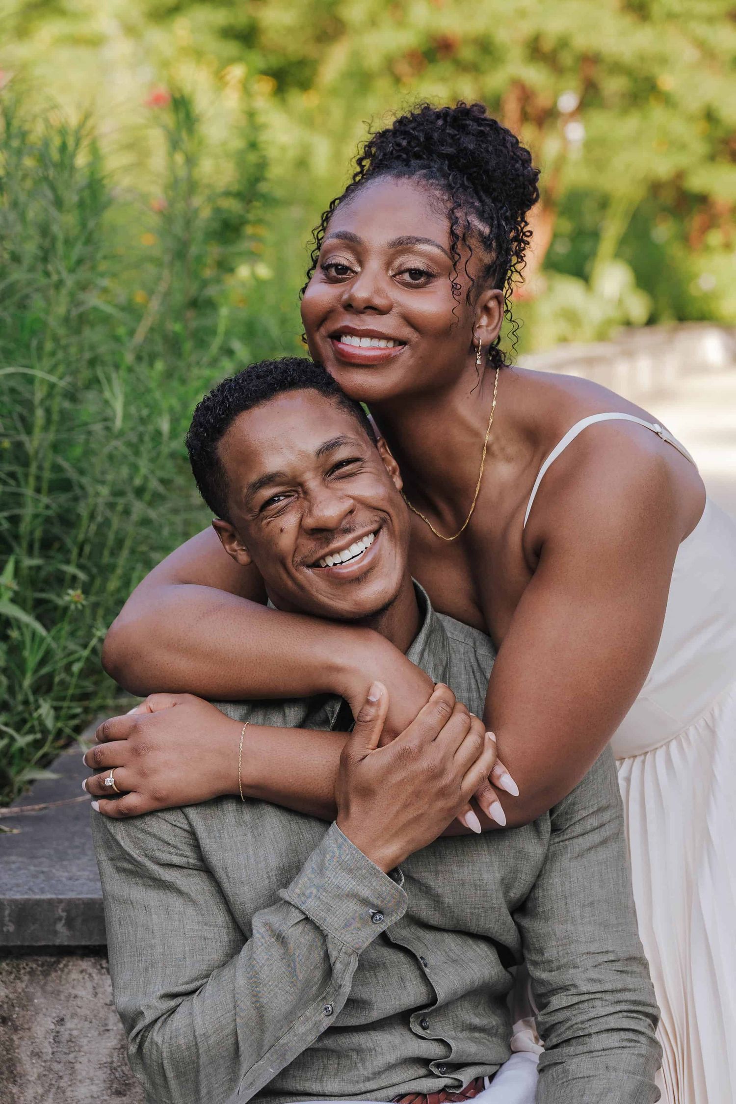 A couple shares a romantic moment in a tree-lined park pathway as they embrace in a joyful lift pose.