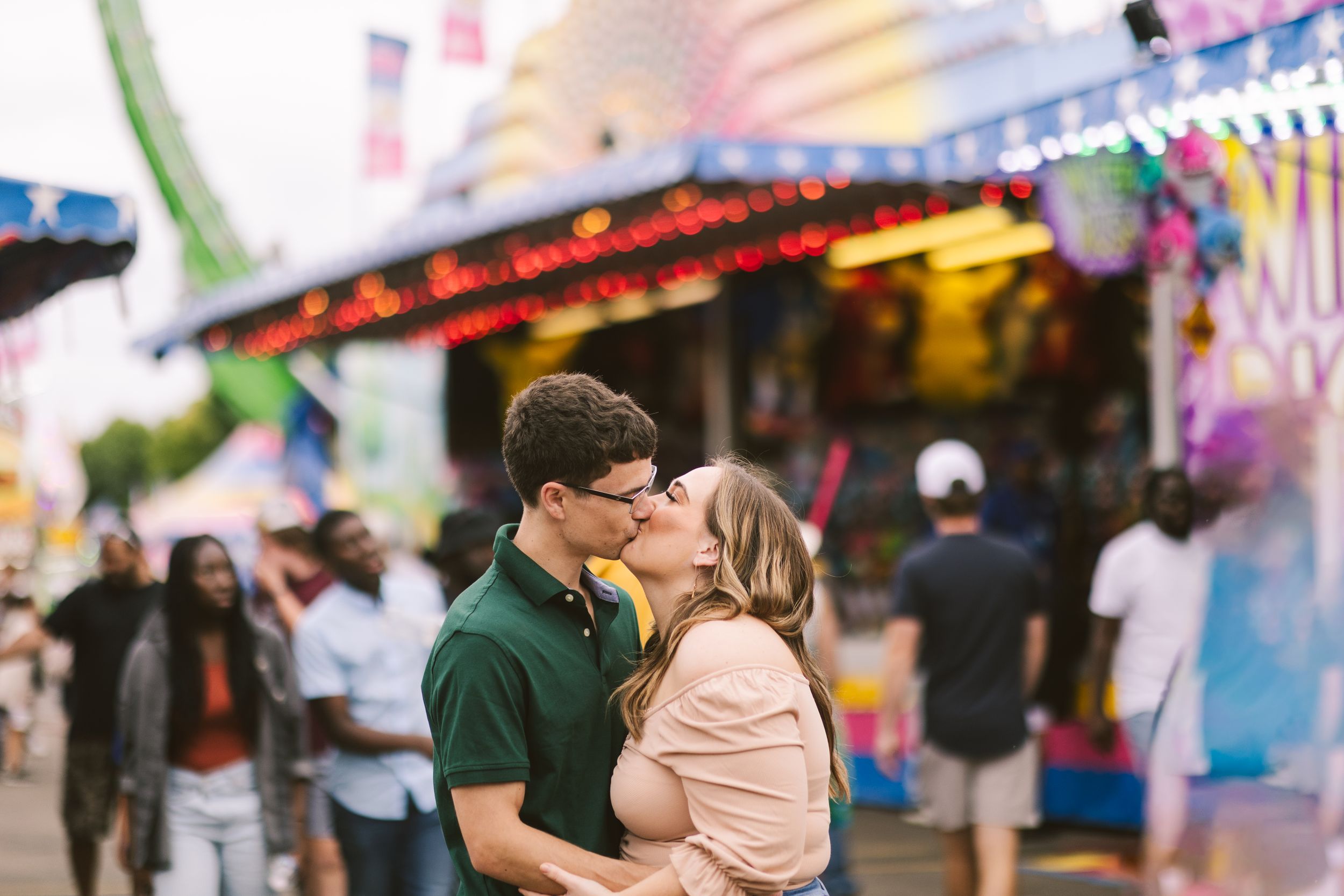 Couple sharing romantic moment at carnival with colorful lights and rides in background. Twin Cities, Decorah Iowa wedding photography