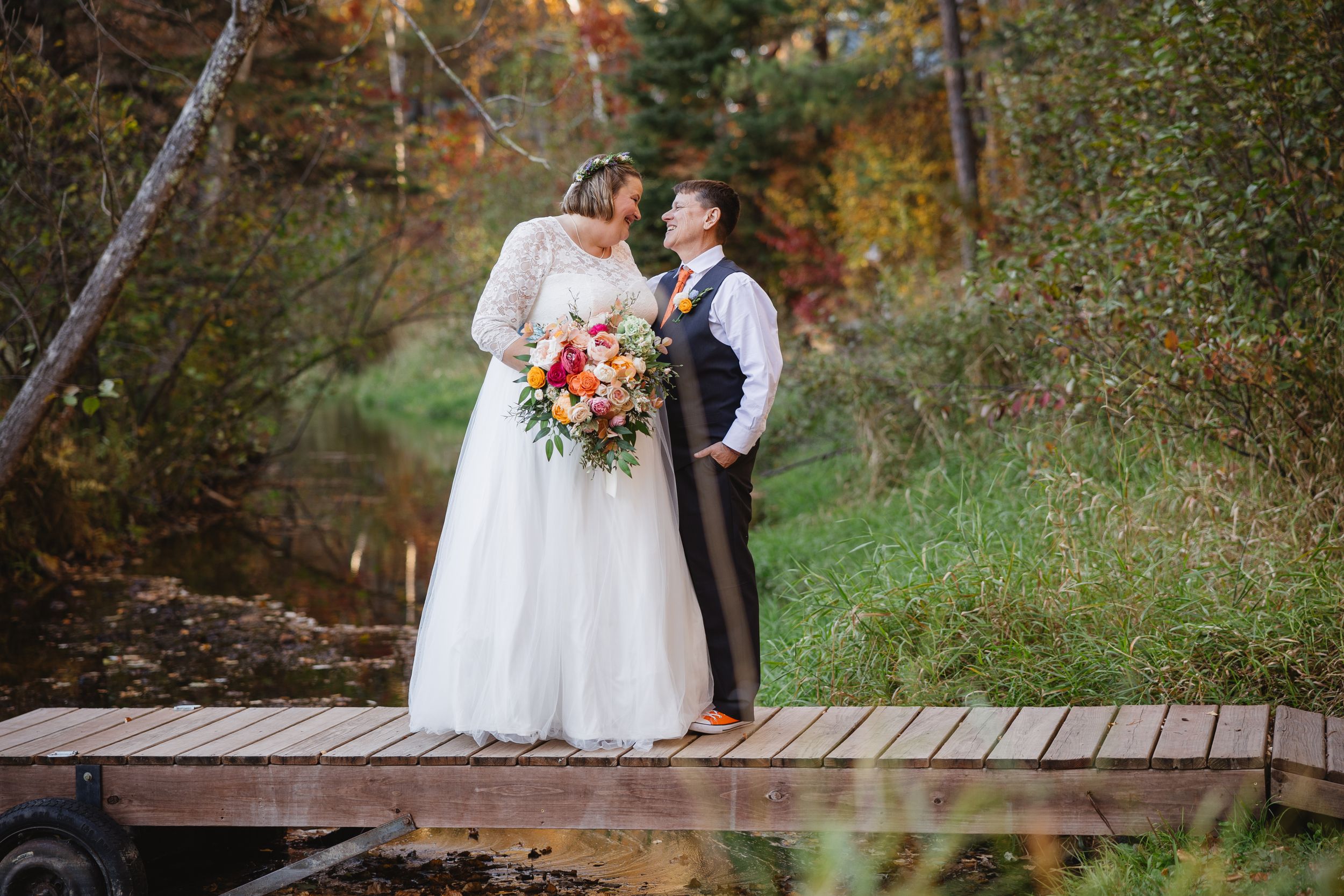 Wedding couple sharing a moment on wooden boardwalk surrounded by autumn foliage.