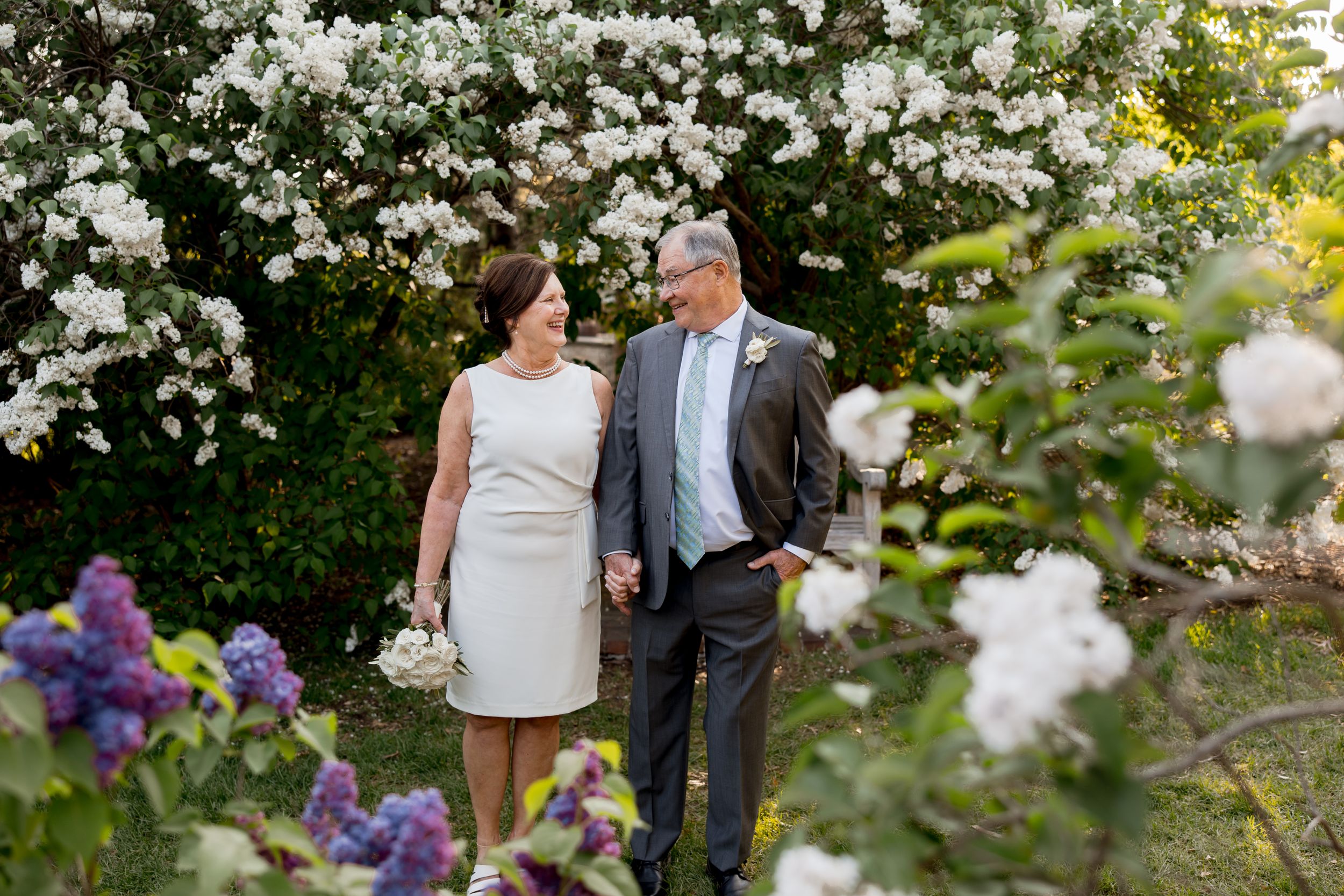 Wedding couple walking through garden with white blooming flowers and purple accents.