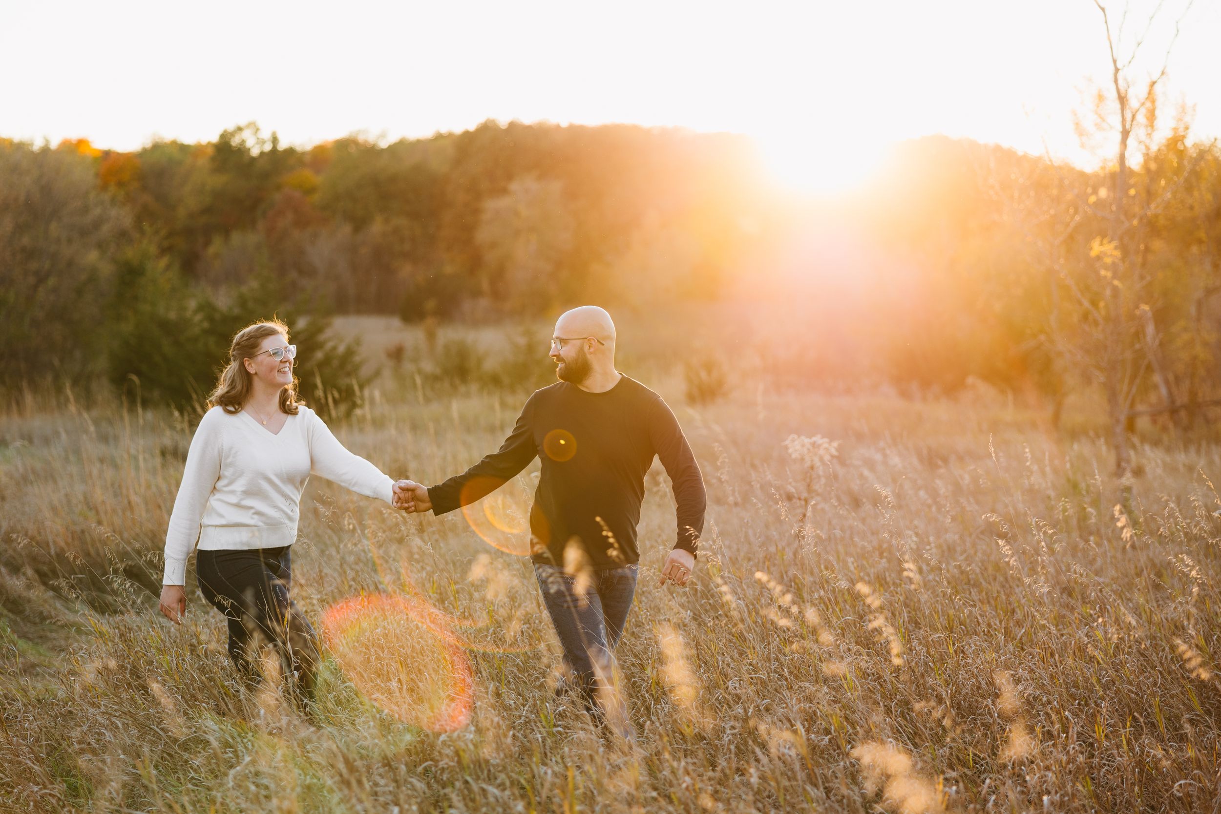 Couple holding hands while walking through golden field at sunset. Twin Cities, Decorah Iowa wedding photography