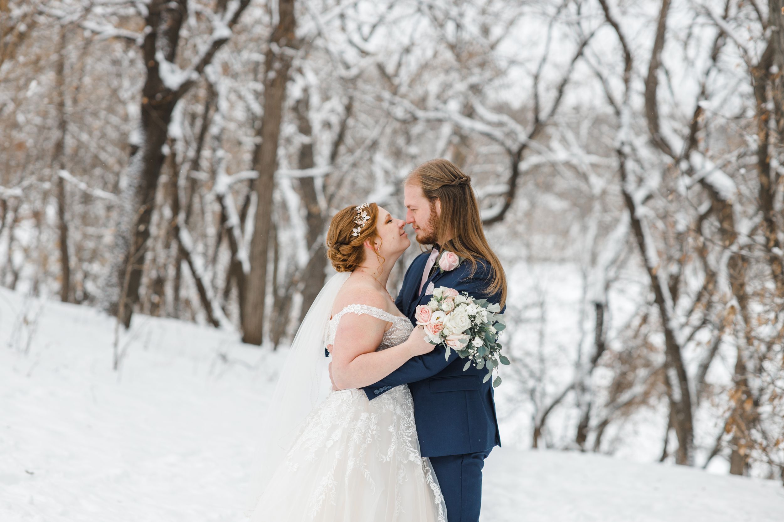 Wedding couple embracing in snowy winter forest setting with white bouquet. Twin Cities, Decorah Iowa wedding photography