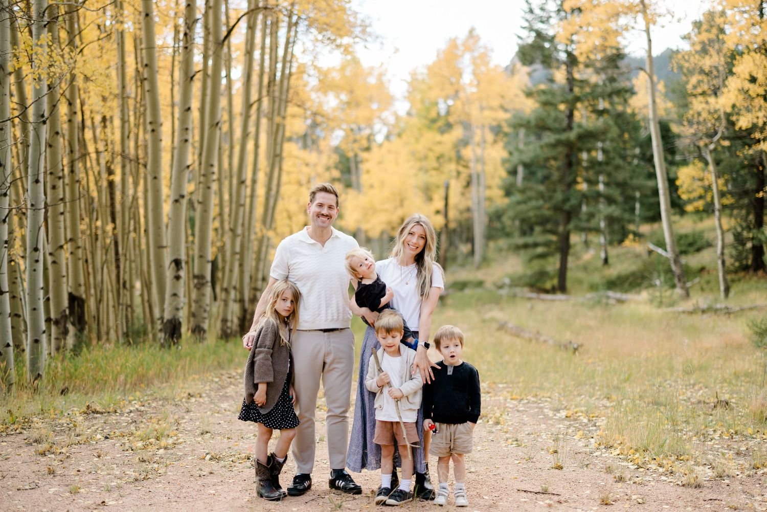 Family of six posing on a dirt path surrounded by golden aspen trees in autumn forest setting.