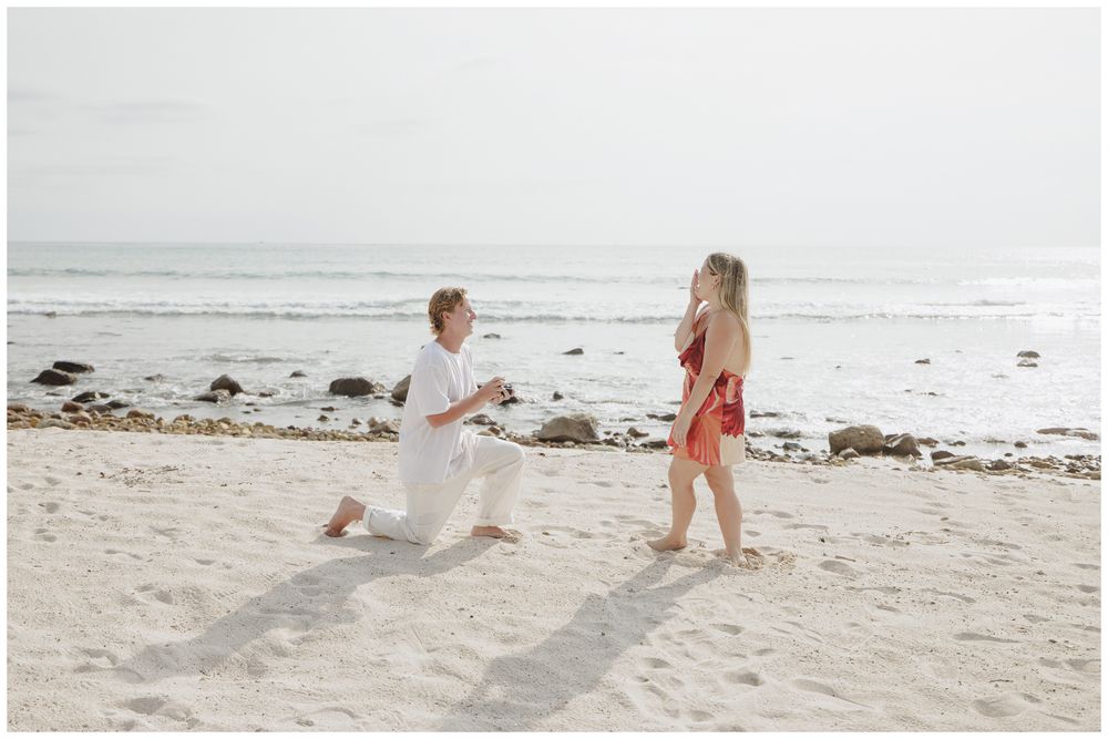 Punta Mita Proposal Photography featuring a Groom proposing on one knee to his bride-to-be on a white sandy beach by the ocean.