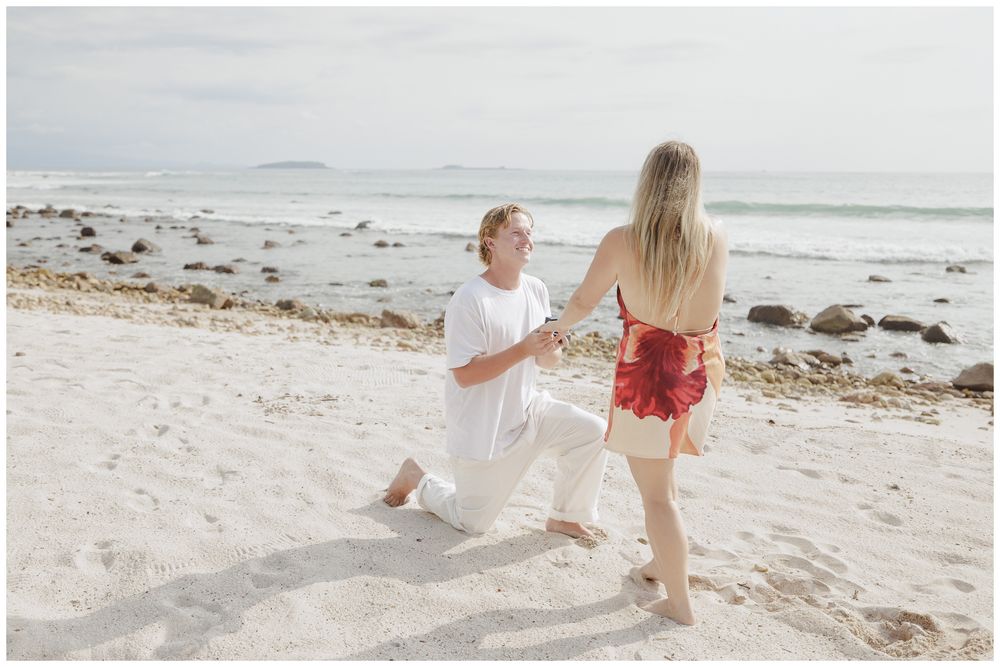 Punta Mita Engagement Session featuring a Groom proposing on one knee to his bride-to-be on a white sandy beach by the ocean.