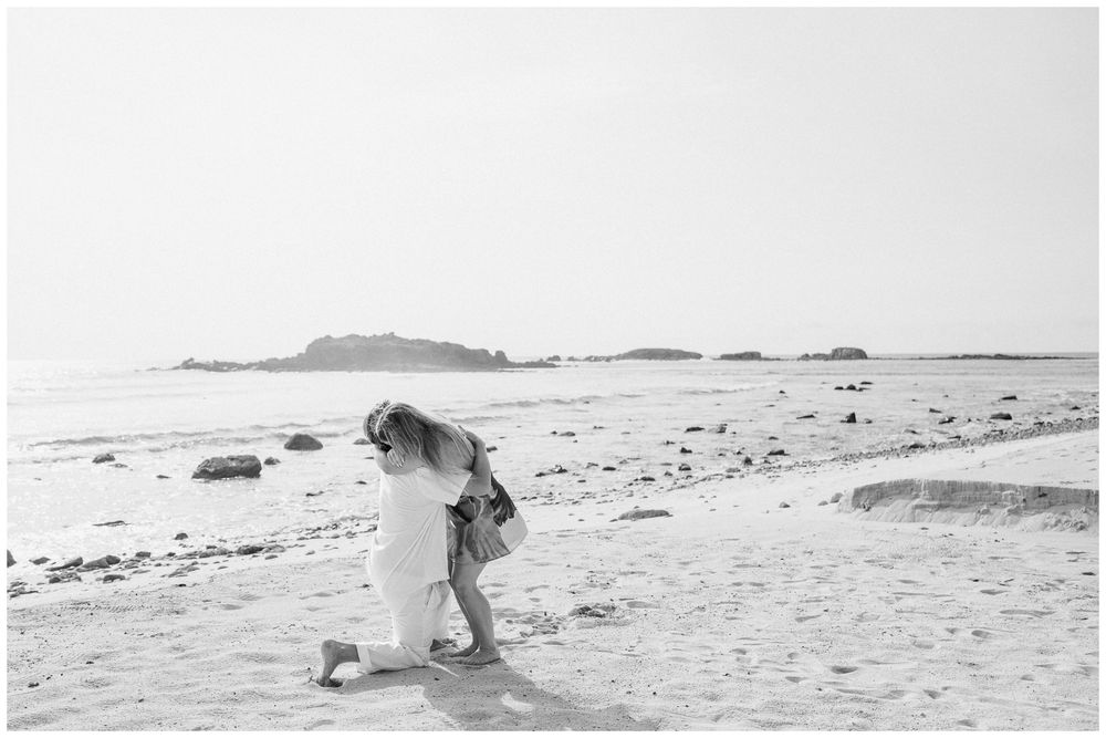 Punta Mita Couple Photo Session featuring a couple embracing on a sandy beach with a rocky shoreline.
